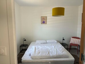 Ett sovrum med en säng, två sängbord, en stol, en lampa och en tavla som hänger på väggen.