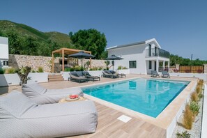 Moderni ulkouima-allasalue, jossa on aurinkotuoleja ja pergola.