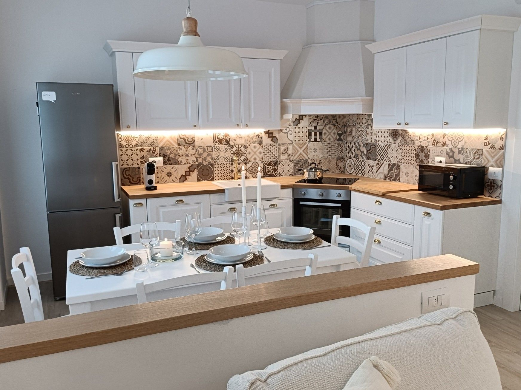 Eine moderne Küche mit weißen Schränken, einer zentralen Kochinsel mit einer Holz Arbeitsplatte und einer gemusterten Spritzschutzeinrichtung.