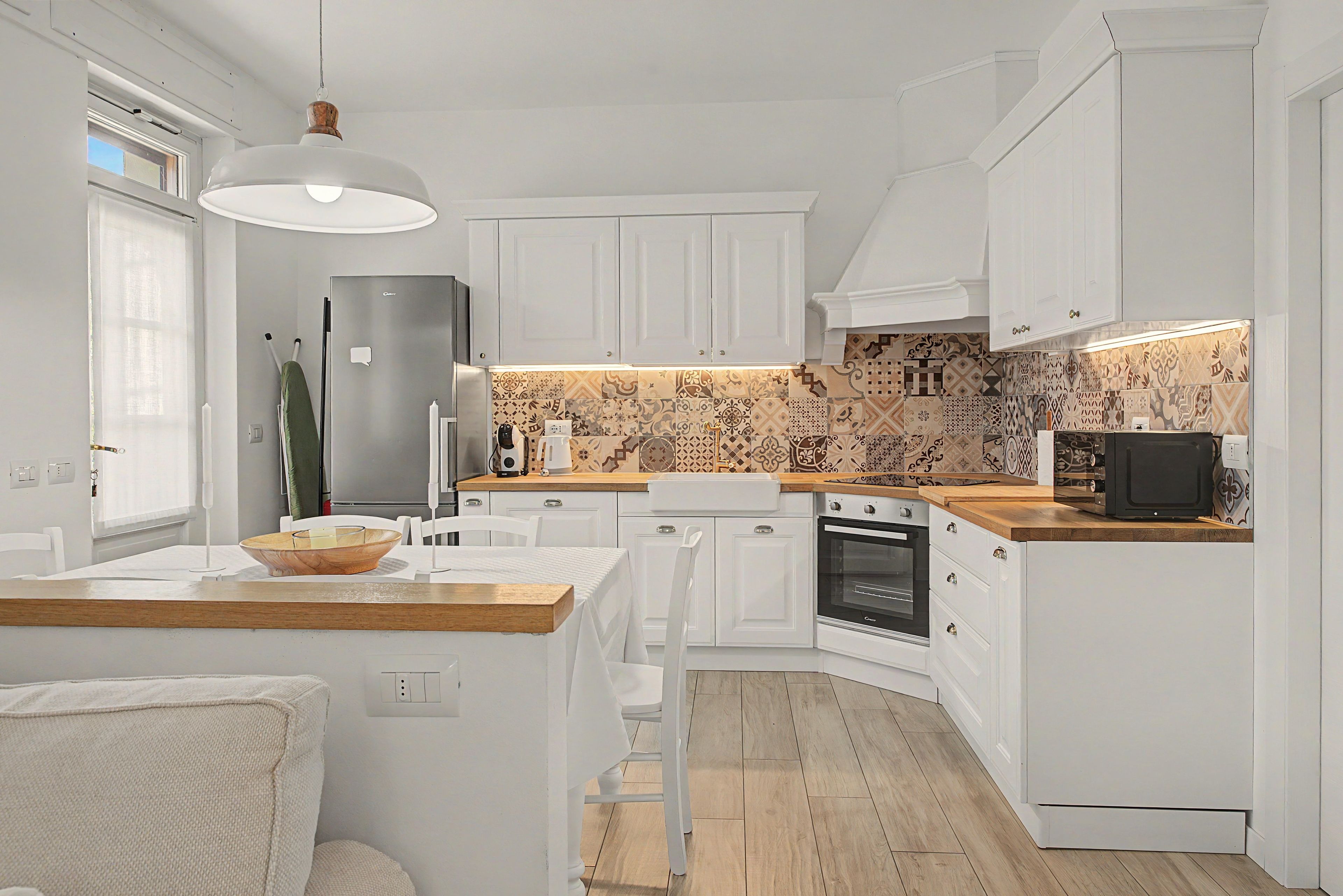 Una cucina moderna con mobili bianchi, un piano di lavoro in legno e una parete di fondo decorata.