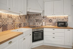 Une cuisine avec des meubles blancs, un four noir, un four à micro-ondes et des carreaux décoratifs sur le mur derrière l’évier.