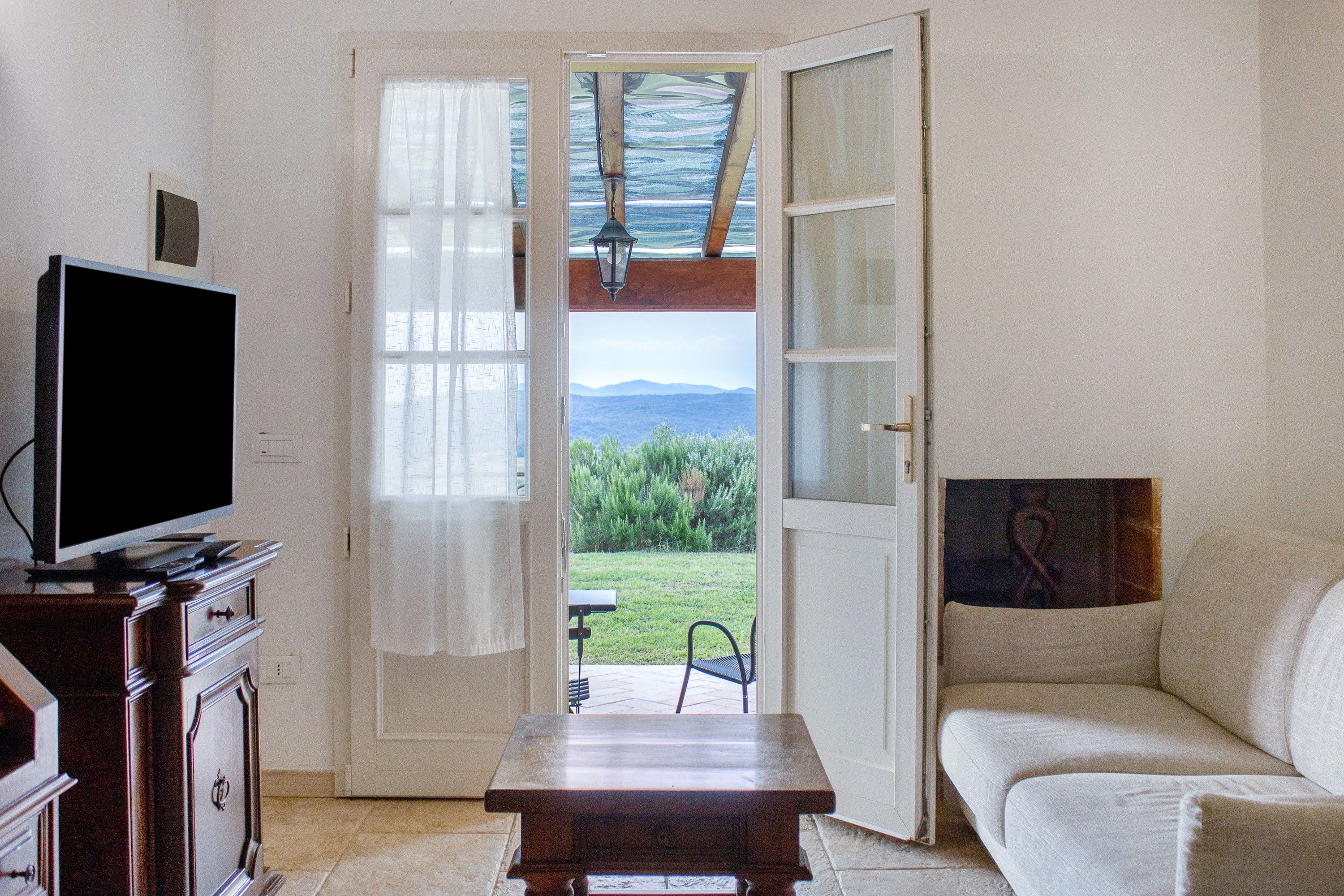 A room with a television on a wooden cabinet, a sofa, and a door leading to a garden.