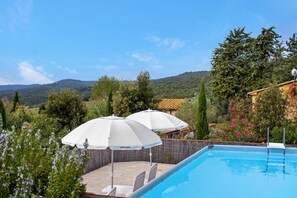 Ein Schwimmbecken mit Blick auf eine gebirgige Landschaft, umgeben von Grünpflanzen und einem Holzzaun.