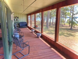 A covered porch with outdoor seating, large windows, and a view of a wooded area. - Welcome to your perfect lakefront getaway! (Avinger)
