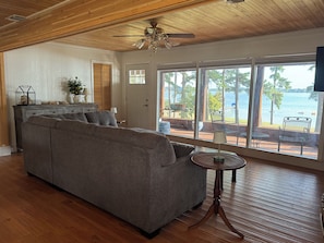 A living room with a grey sofa, a wooden ceiling, and a view of a lake through large windows. - Welcome to your perfect lakefront getaway! (Avinger)