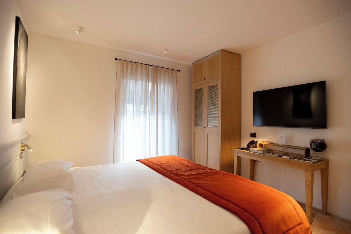 A hotel room with a bed, a desk with a television, and a window with curtains.