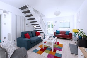 A modern living room with a staircase, two sofas, a coffee table, and a colorful rug. - Seaweed (Combe Martin)