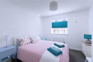 Ein Schlafzimmer mit Bett, Nachttisch, Kommode, einem Fenster mit Jalousien und einer Hängeleuchte.