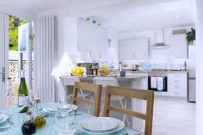 A modern kitchen with white cabinets, a dining area with a table set for two, and a view of the outdoors. - Seaweed (Combe Martin)