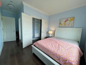Un dormitorio con cama, mesita de noche, lámpara, armario y un cuadro en la pared.