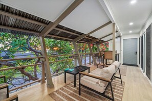 Ein moderner Balkon mit Holzboden, einer Couch, einem Tisch und Blick auf üppiges Grün.