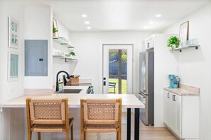 A modern kitchen with white cabinetry, a stainless steel refrigerator, and two wicker chairs. - Kahaluu Beach Surf, Oceanview, 2bed,2bath, Lanai (Kailua-Kona)
