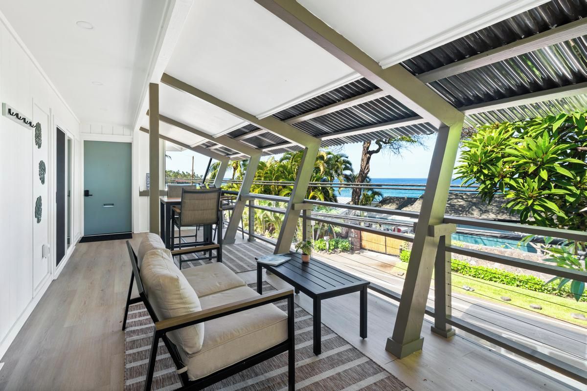 A modern outdoor seating area with a view of the ocean, featuring a sofa, a table, and a railing.