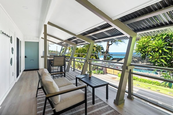 Uma área de estar moderna ao ar livre com vista para o oceano, incluindo um sofá, uma mesa e um corrimão.