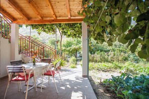 Um pátio externo com pérgola de madeira, uma mesa com cadeiras e vista para um jardim e colinas ao fundo.