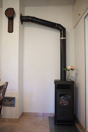 A room with a black wood-burning stove, a wall-mounted clock, and a vent pipe. - House with large garden, right next to the river (Žrnovnica)