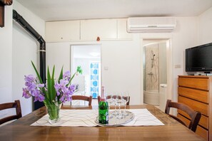 Uma área de refeições com uma mesa posta para seis pessoas, uma garrafa verde e um vaso de flores roxas.