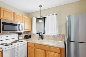 A kitchen with wooden cabinets, a stainless steel refrigerator, a microwave, a stove, and a coffee maker. - Royal Kahili Oceanview Condo Sleeps 6 AC + Lanai (Kailua Kona)