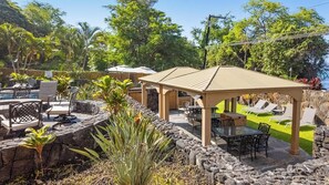 Un espace extérieur aménagé en terrasse, doté d’un coin salon couvert, de murs en pierre et offrant une vue sur l’océan.
