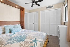 Ein Schlafzimmer mit einem Bett, einem Deckenventilator, weißen Schränken und einem Fenster.