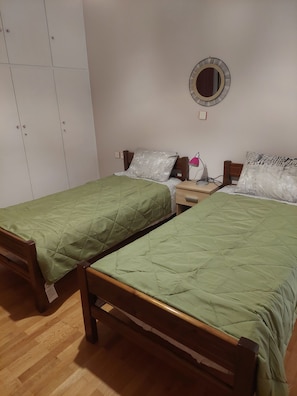 Ein Zimmer mit zwei Einzelbetten, einem Nachttisch mit Lampe, einem Spiegel an der Wand und einem Kleiderschrank.