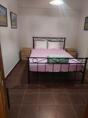 Ein Schlafzimmer mit einem Metallbettgestell, einer rosa Bettdecke, zwei Nachttischen und einem Holznachttisch.