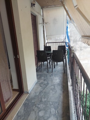 A covered outdoor seating area with a table and chairs, a metal railing, and a view of the outside.