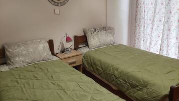 A bedroom with two single beds, a bedside table with a lamp, a mirror on the wall, and a floral curtain.