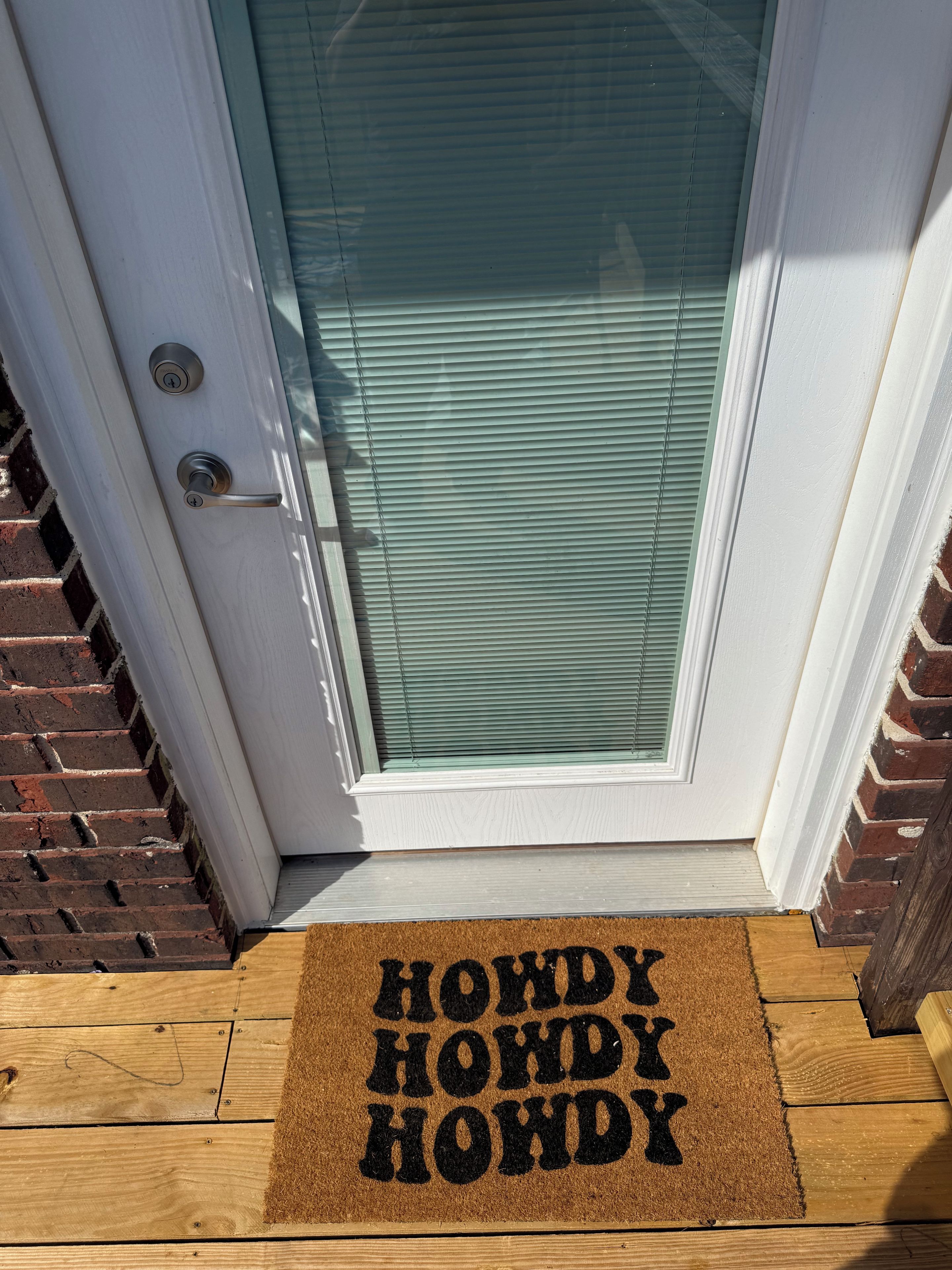 A door with a glass panel and a doormat with 'HOWDY HOWDY HOWDY' text.