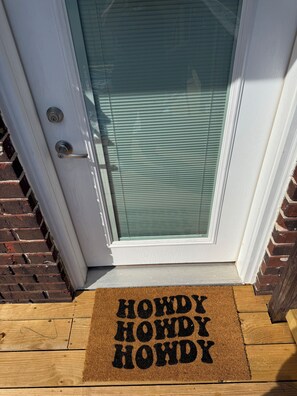 Puerta con panel de vidrio y felpudo con la inscripción 'HOWDY HOWDY HOWDY'.