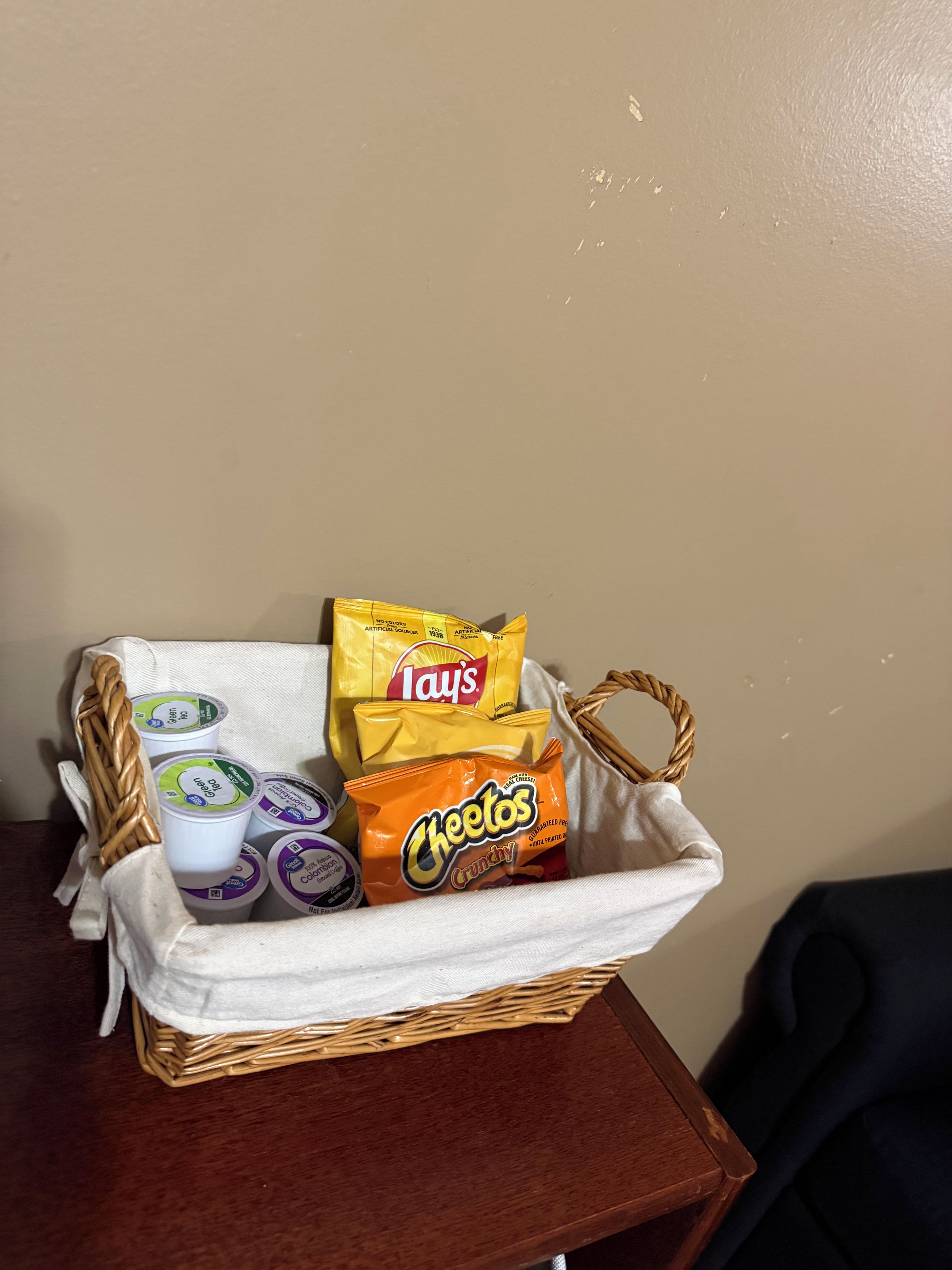 A wicker basket containing Lay's chips, Cheetos, and yogurt cups on a wooden table.