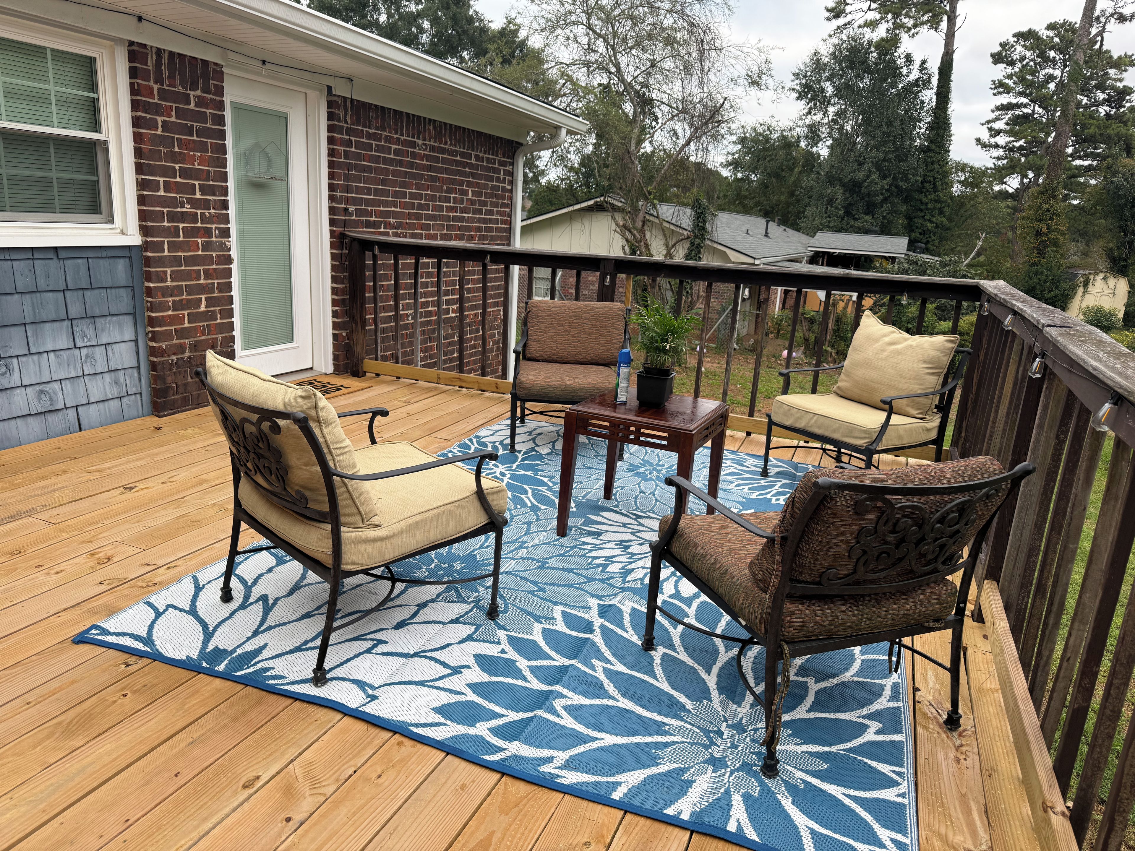 A wooden deck with outdoor furniture, including two chairs and a table, and a decorative rug.