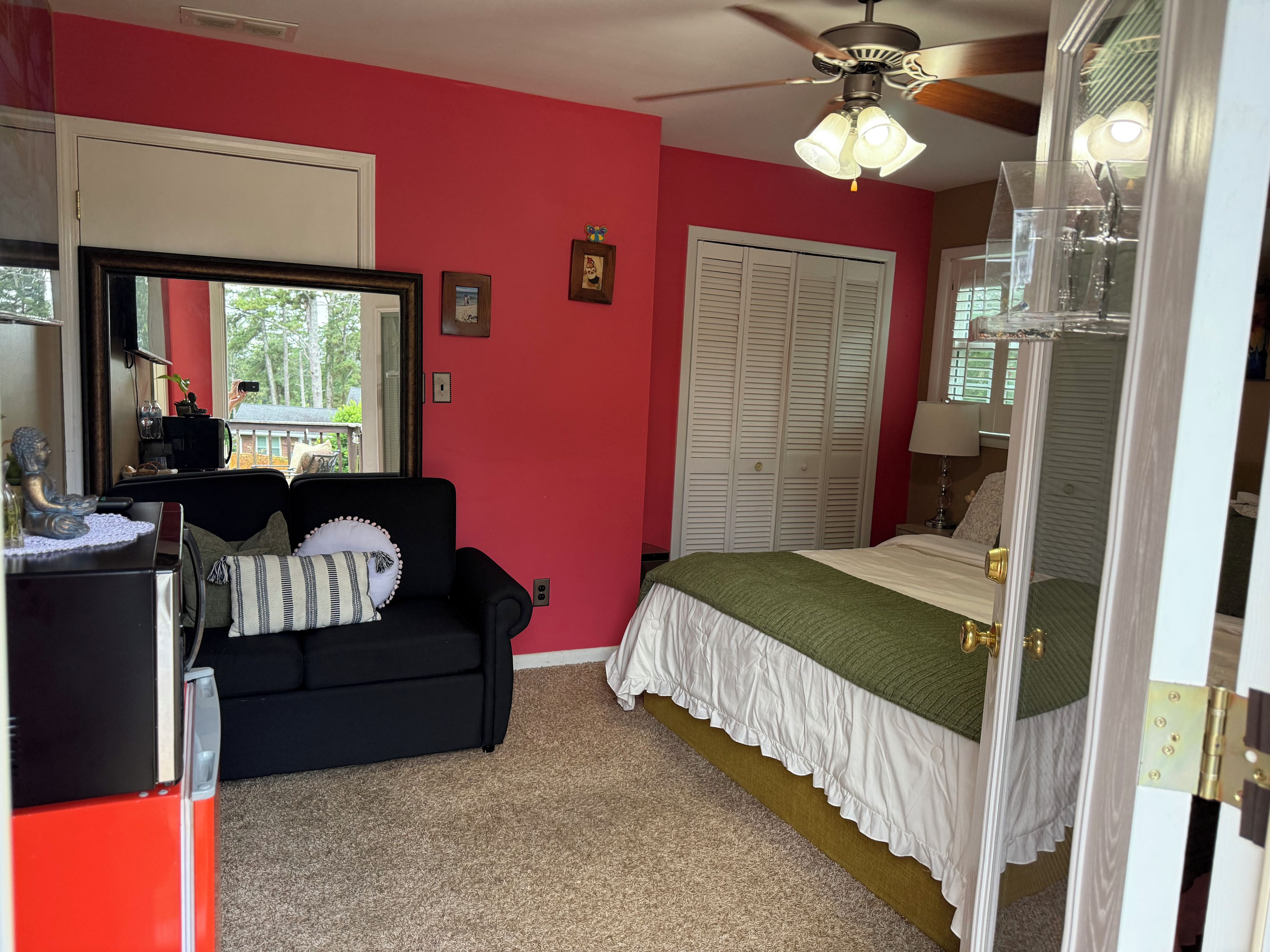 A bedroom with a black sofa, a bed with a green bedspread, a ceiling fan, and a large window.