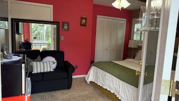 A bedroom with a black sofa, a bed with a green bedspread, a ceiling fan, and a large window.