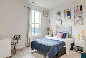 A modern bedroom with a bed, bedside tables, a desk, and artwork on the walls.