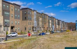 Row of modern multi-story townhouses along a paved road under a bright sky.
