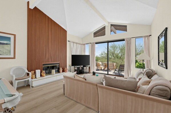 Ein modernes Wohnzimmer mit Fernseher, einer Couch, einem weißen Sessel und einem Kamin.