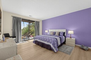 Ein Schlafzimmer mit einem großen Bett, einem Nachttisch, einem Sessel und Blick auf einen Garten durch eine Schiebetür.
