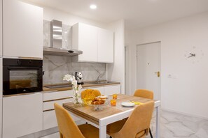 Een moderne keuken met witte kasten, een inbouwoven en een eettafel met stoelen.