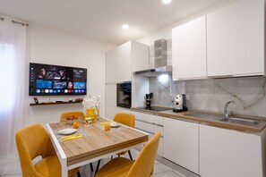 Eine moderne Küche mit integriertem Backofen, einer Kaffeemaschine und einem an der Wand montierten Fernseher, der verschiedene Sender zeigt.