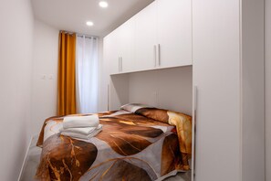 A single bed with a patterned bedspread, a folded towel, and a window with curtains. - Cavour Lake Apartments – Ambra
Appartamento centrale Intra (Pallanza)