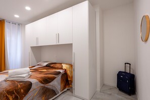 Ein Schlafzimmer mit einem Bett, einem Kleiderschrank, einem Koffer und einem Spiegel an der Wand.
