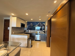 Una cocina moderna con encimeras de granito, electrodomésticos de acero inoxidable y una zona de comedor con mesa de vidrio.