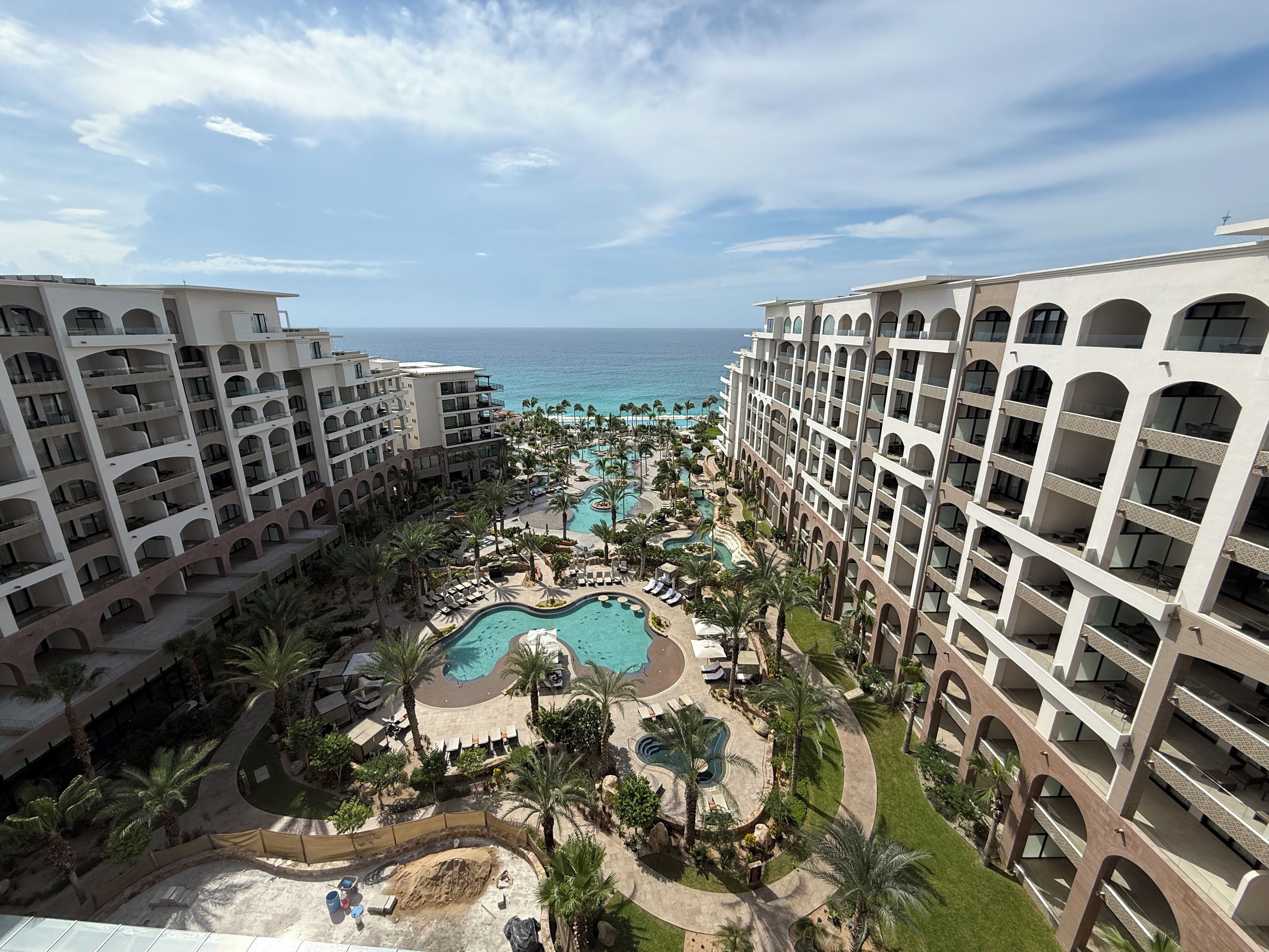 A resort with multiple buildings, a central swimming pool, and a view of the ocean.