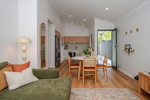 A compact living space with a dining area, kitchenette, and a cozy seating area with a lamp and cushions. - Olive & Ochre | Warm Coastal Retreat (Shoalwater)