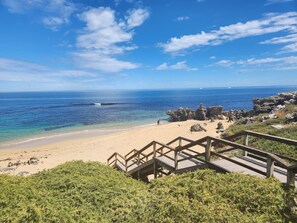 Une plage avec un escalier en bois descendant jusqu’au rivage, un ciel bleu clair et une mer calme.