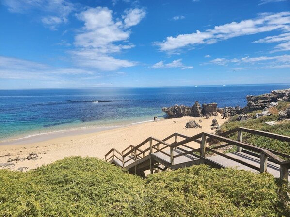 Ein Strand mit einer Holztreppe, die zum Ufer führt, wolkenloser, blauer Himmel und ruhiges Meer.