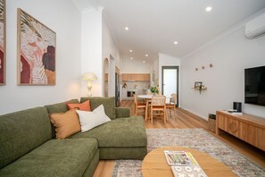 Un salon moderne avec un canapé d’angle, une table à manger avec des chaises et un téléviseur posé sur un meuble en bois.