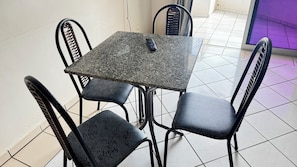 Una mesa cuadrada con un control remoto, rodeada por cuatro sillas con un diseño de hojas.
