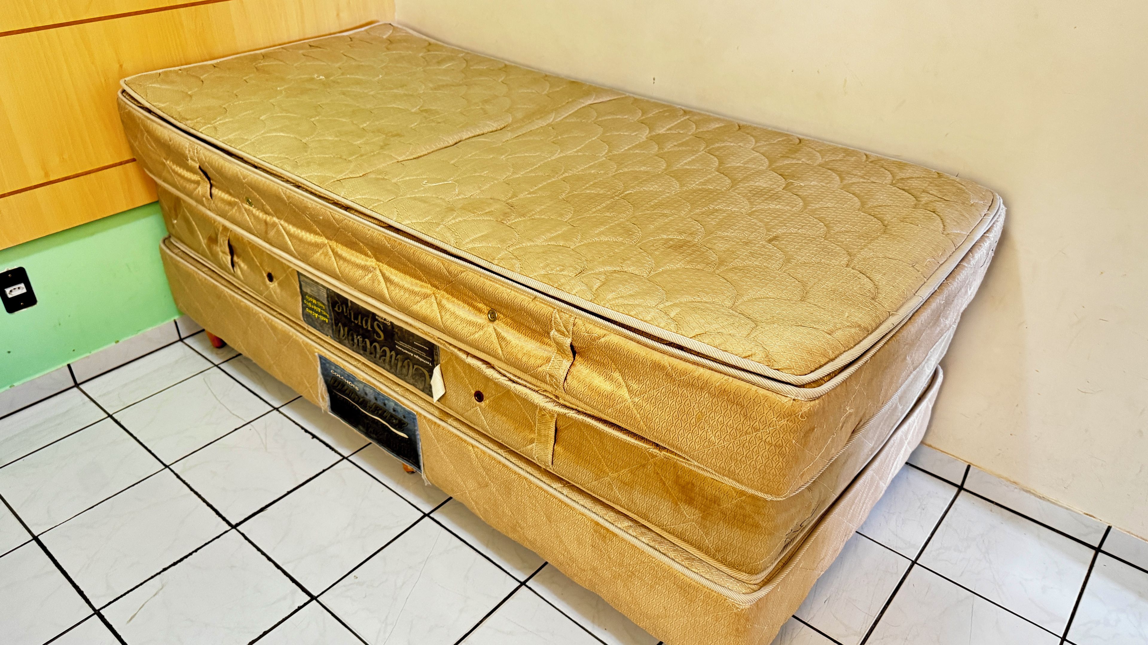 Um colchão grande, cor de ouro, com topo acolchoado, sobre um chão de azulejos.